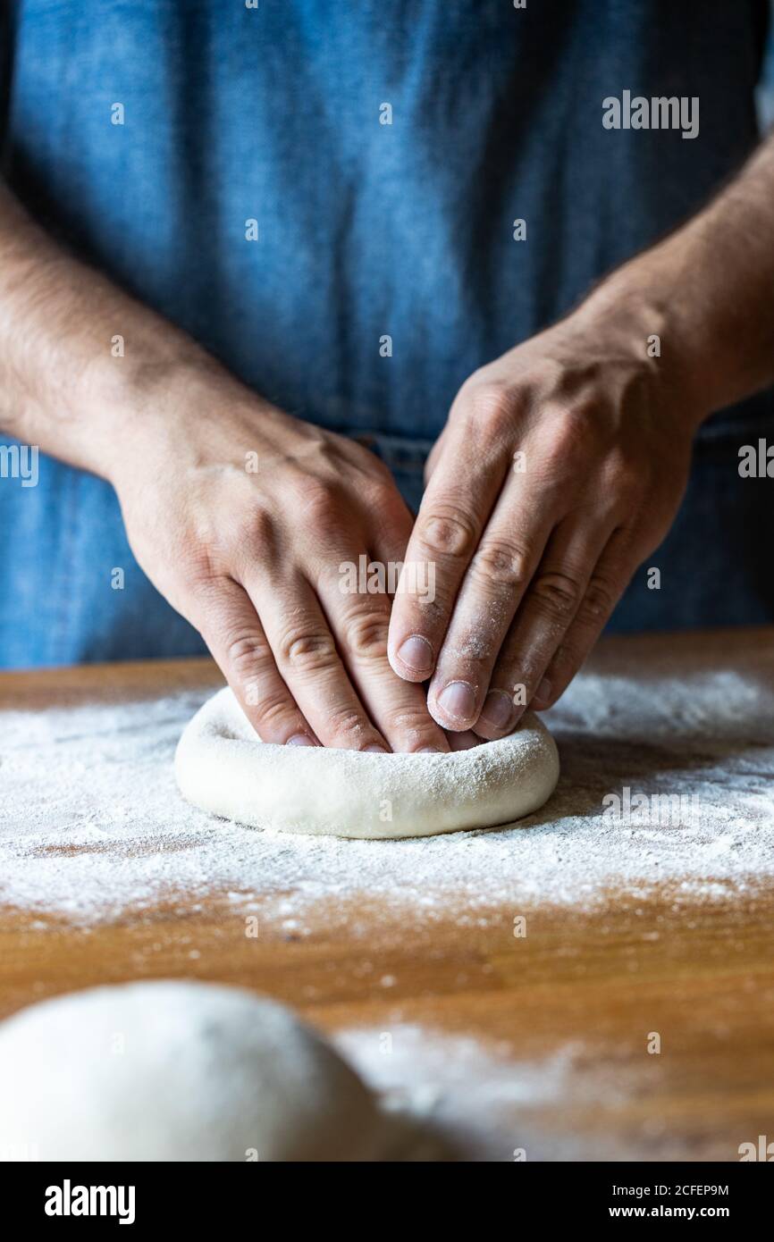 Unkenntlich Männchen in Schürze Abflachung weichen Teig über Tisch mit Mehl beim Kochen Pizza Stockfoto