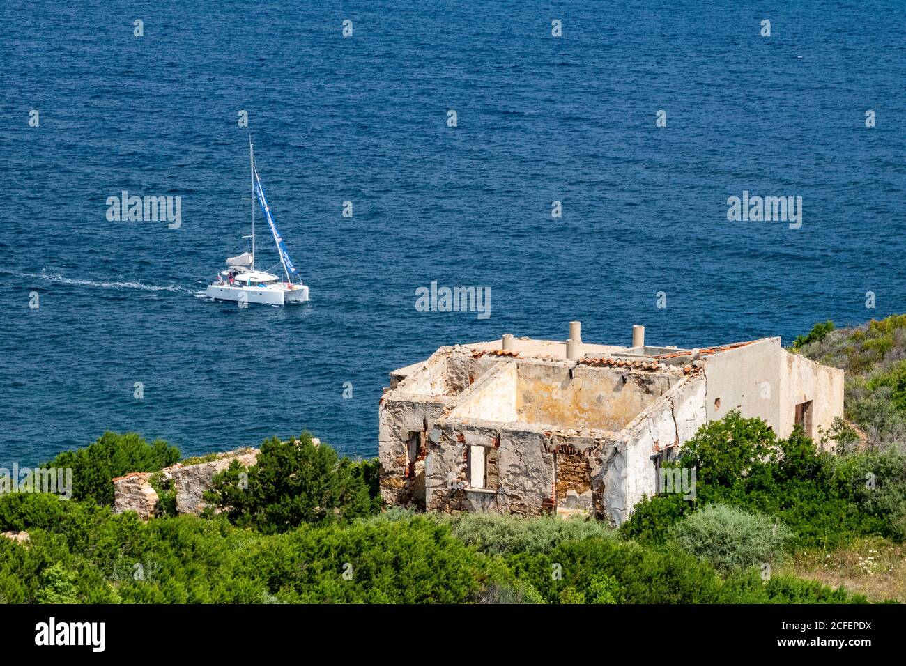 Bunte Blick auf die Küste von Nord-Sardinien mit Katamaran und Ruine von Batteria Battistoni– Baia Sardinia, Costa Smerelda, Sardinien, Italien. Stockfoto