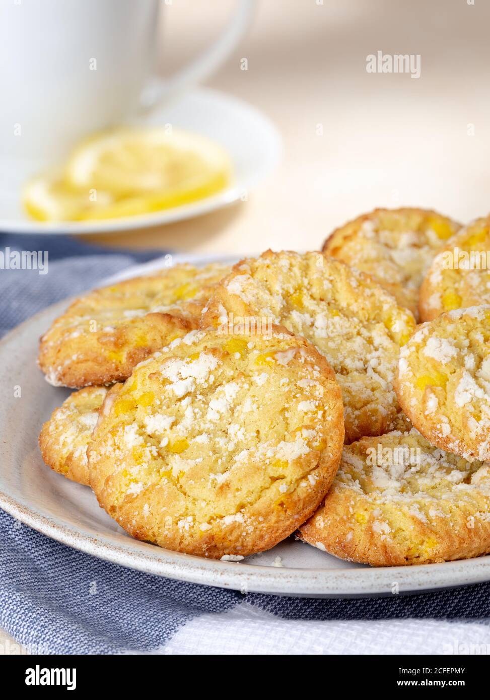 Zitronencrinkle Kekse auf einem Teller mit Tasse und in Scheiben geschnitten Zitrone im Hintergrund Stockfoto