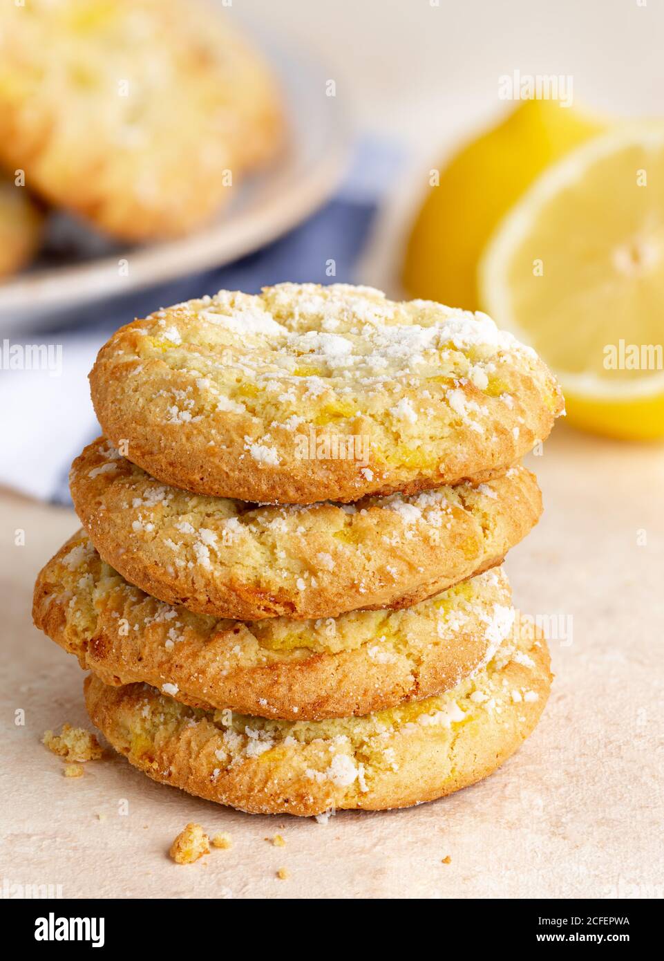 Stapel von Zitronencrinkle Cookies auf einem Tisch mit in Scheiben geschnitten Zitrone und Keksplatte im Hintergrund Stockfoto