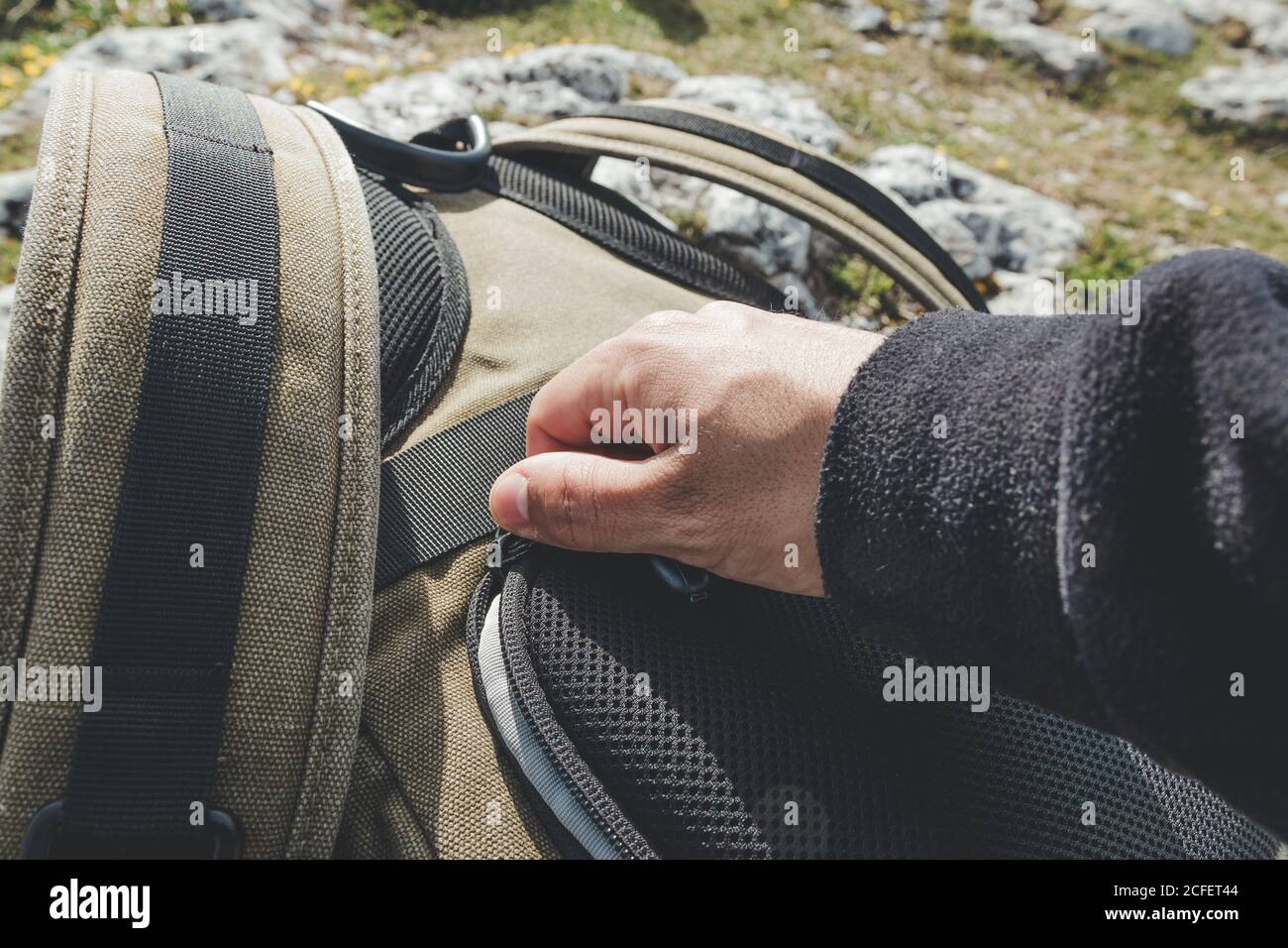 Crop Mann Hand in warmen Pullover Zipping up Reiserucksack Auf Reise bei sonnigem Wetter Stockfoto