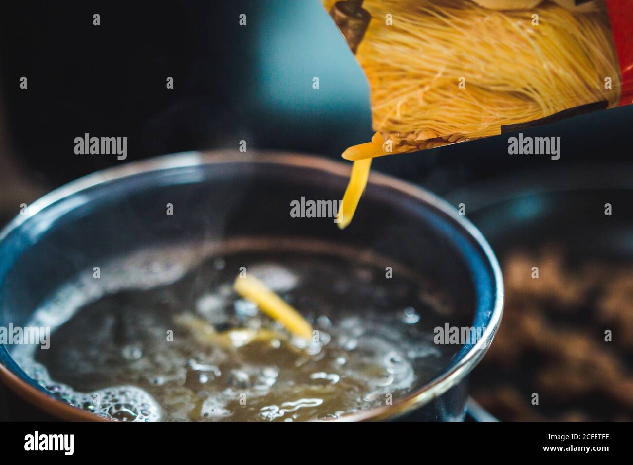 Closeup rohe Pasta verschüttet aus der Box in den Topf mit kochendem Wasser bei der Zubereitung von Speisen in der Küche Stockfoto