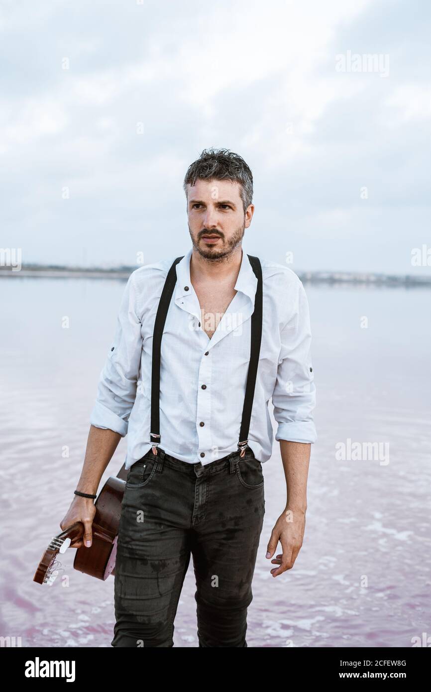 Mann in weißem Hemd und Hosenträger, der Gitarre hält, während er barfuß am  Ufer im Wasser steht Stockfotografie - Alamy