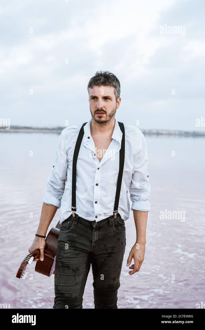 Mann in weißem Hemd und Hosenträger halten Gitarre im Stehen Barfuß im  Wasser am Ufer an bewölktem Tag Stockfotografie - Alamy