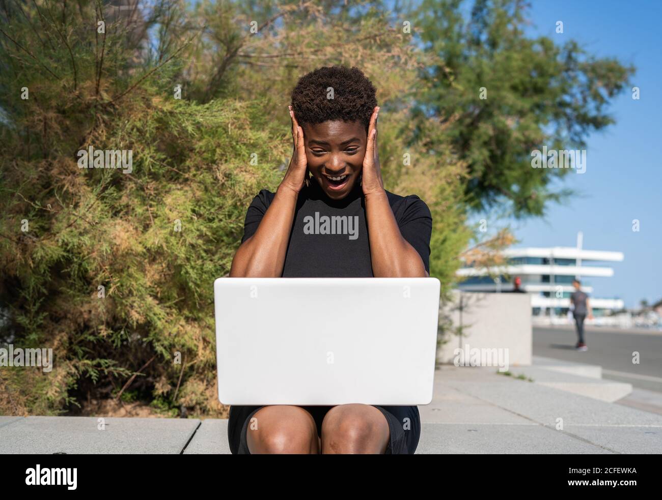 Fröhlich aufgeregt Frau in elegantem schwarzen Kleid mit Laptop, während auf dem Bürgersteig auf der Straße entspannen Stockfoto