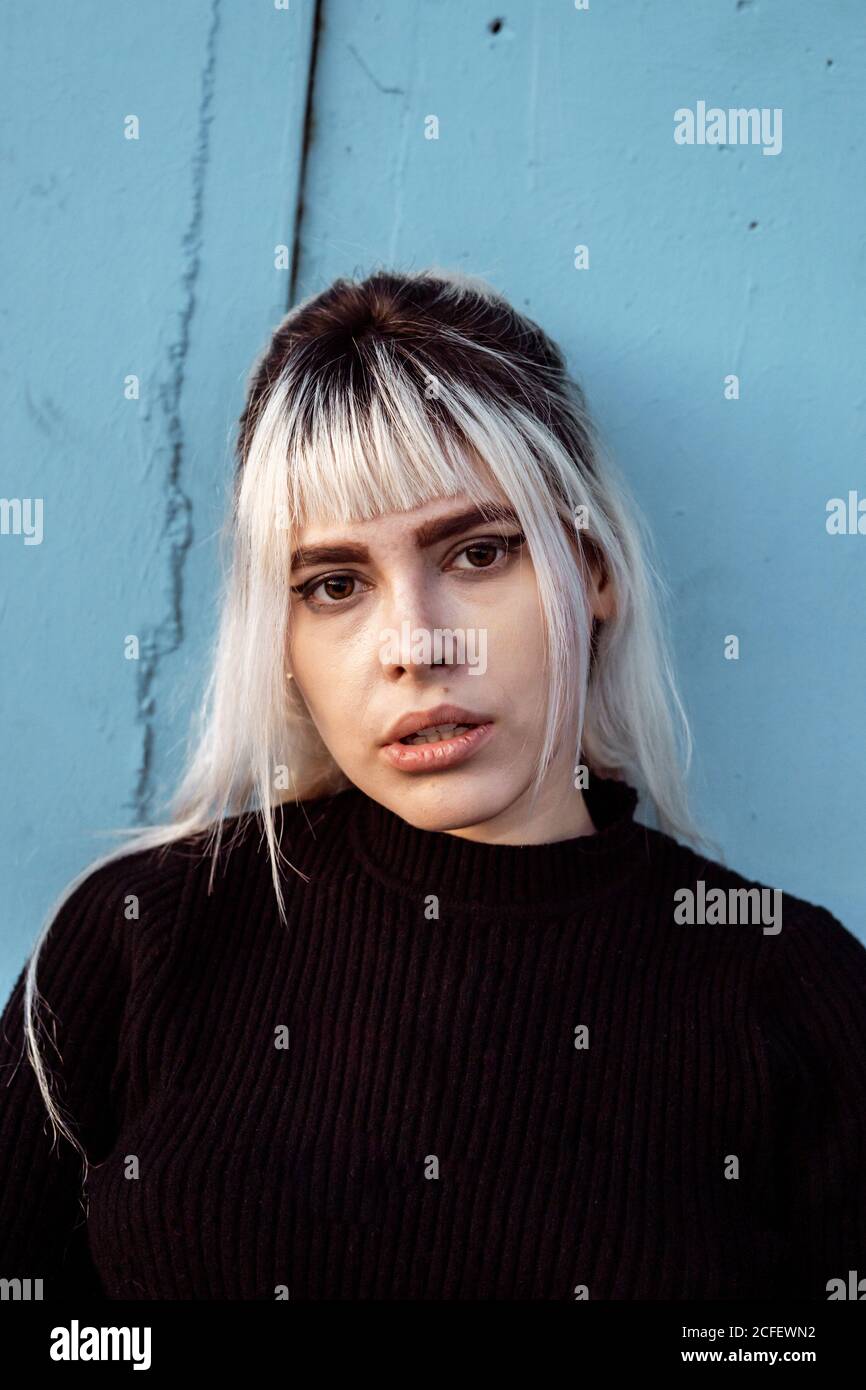 Junge blonde Frau mit langen blonden Haaren trägt schwarzen Pullover Blick auf die Kamera mit unglücklichen und enttäuschten Augen müde Gesicht Stockfoto