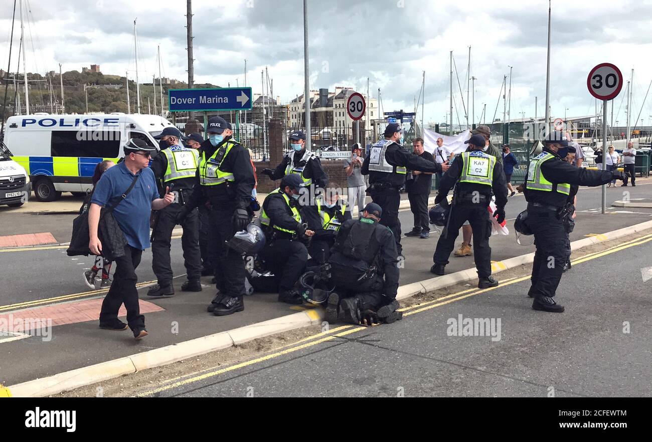 Ein Mann, der von der Polizei am Boden festgehalten wird, wird verhaftet, während andere Beamte eine Absperrung schaffen, um Anti-Migrantenprotestierende, die in Dover gegen die Einwanderung und die Reisen von Flüchtlingen, die den Kanal nach Kent überqueren, aufzuhalten. Stockfoto