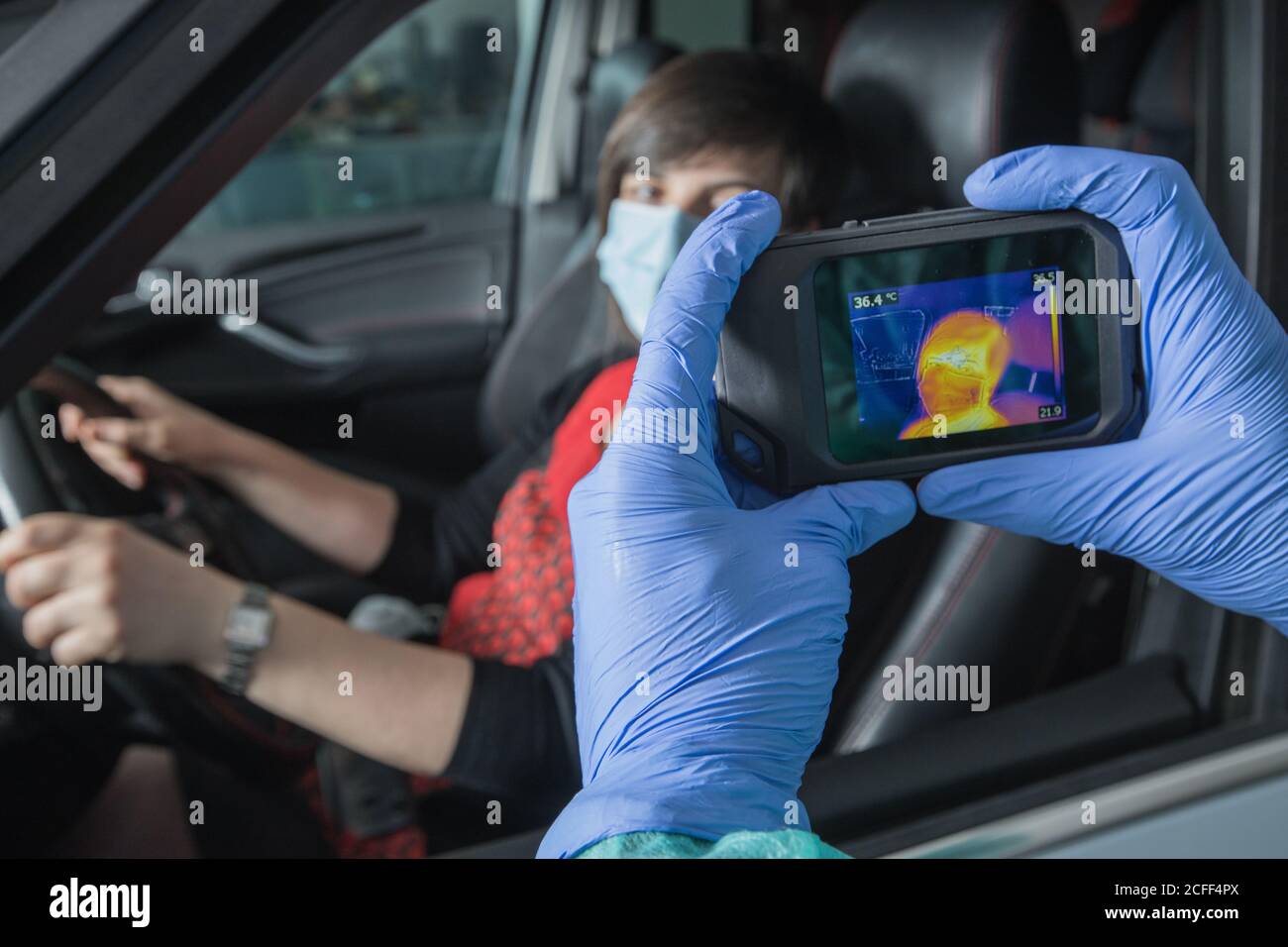 Crop Arzt in medizinischen Handschuhen Messung der Temperatur der weiblichen Fahrer Bei der Verwendung von Infrarotkamera während Coronavirus-Epidemie Stockfoto