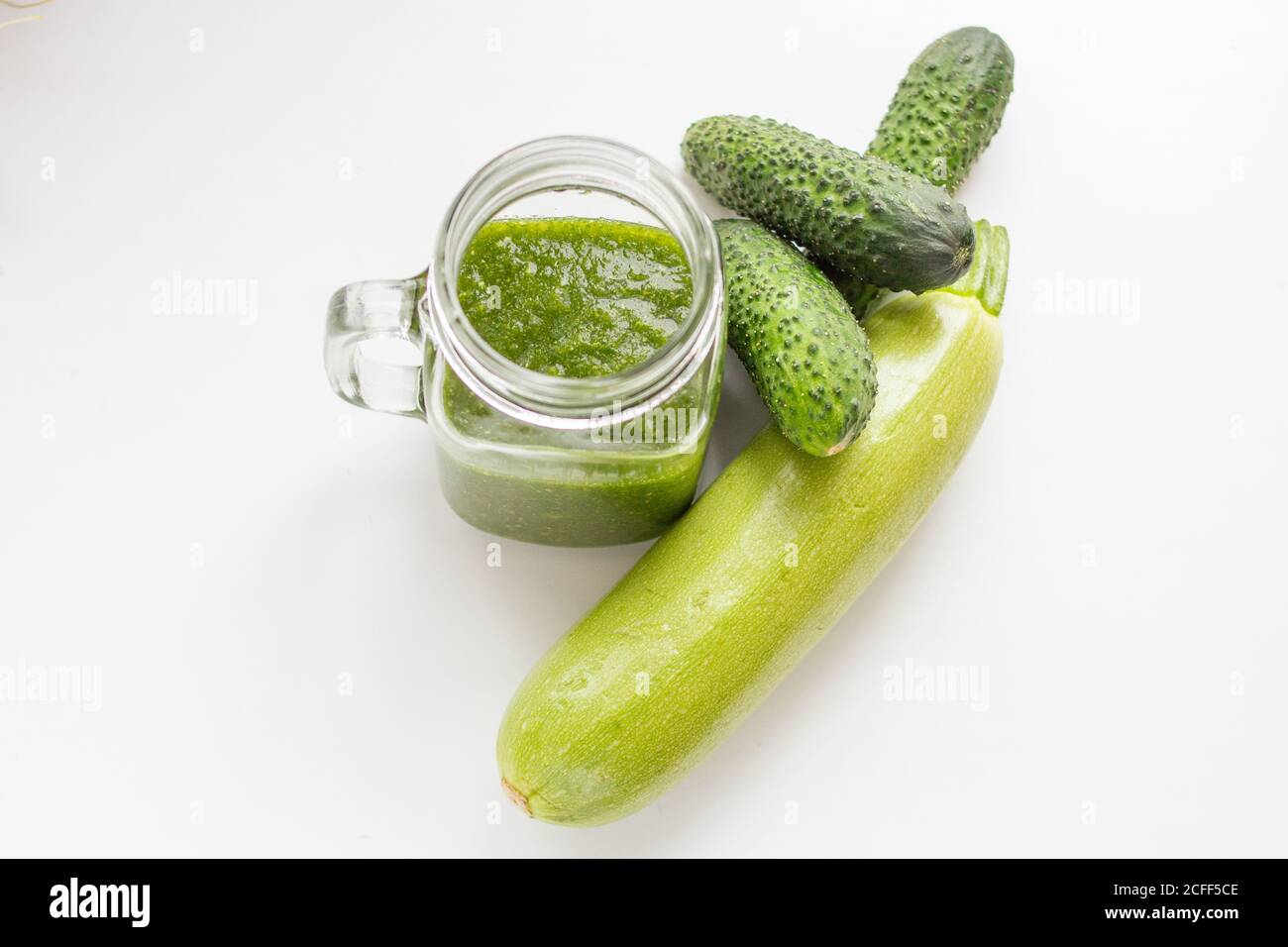 Grüner roher Smoothie in einer Glastasse und grünes Gemüse. Gurken und Zucchini Stockfoto