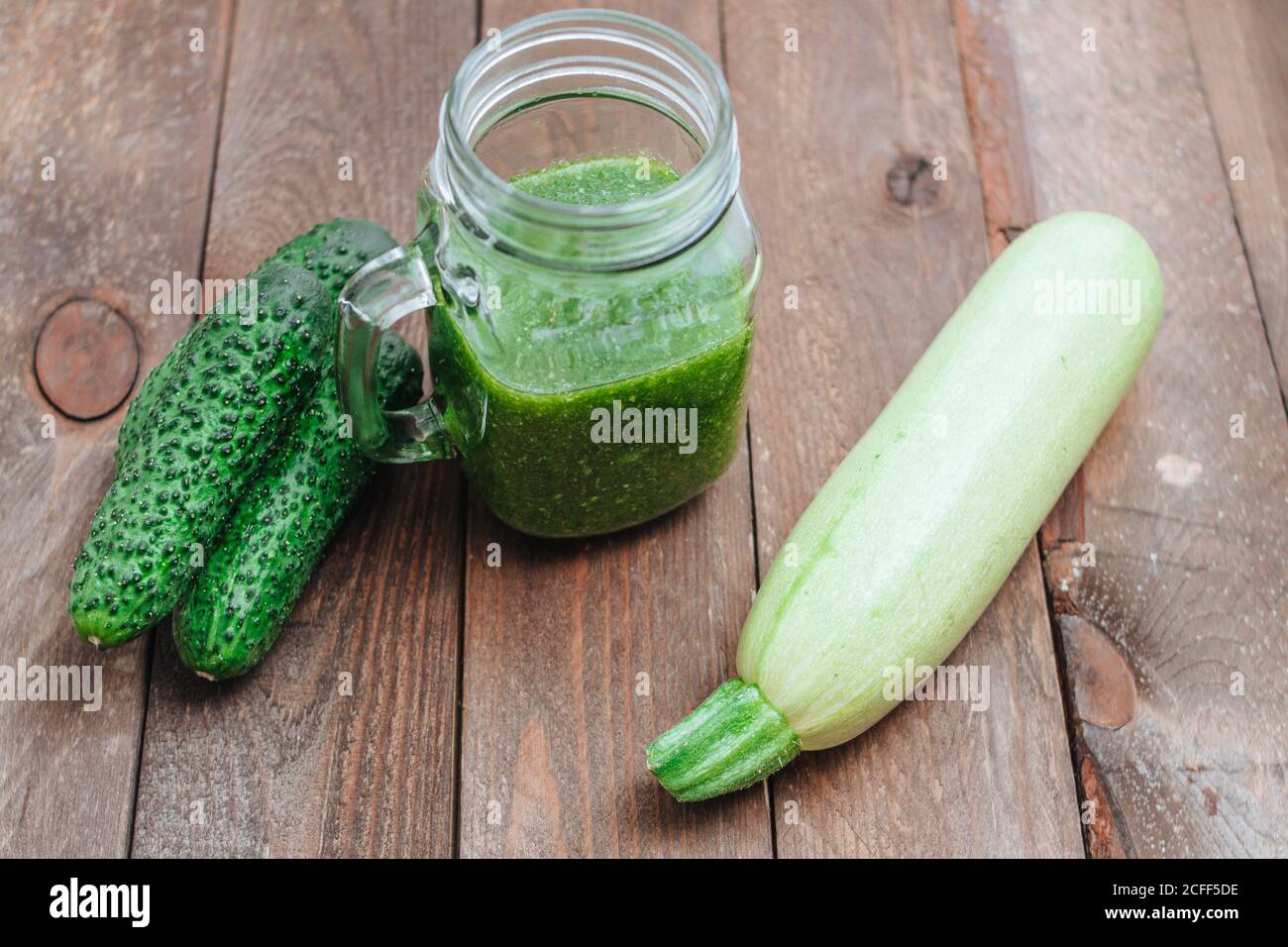 Grüner roher Smoothie im Glas und grünes Gemüse auf Holzbrettern. Gurken und Zucchini Stillleben Stockfoto
