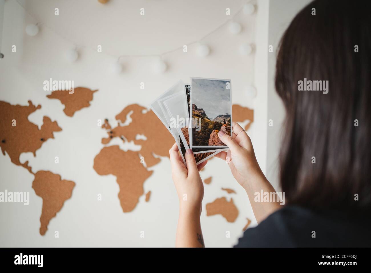 Crop Rückansicht von gesichtslosen weiblichen Touristen beobachten Bilder und Erinnerung an vergangene Reise, während Sie vor der Weltkarte stehen Zu Hause in Paris Stockfoto