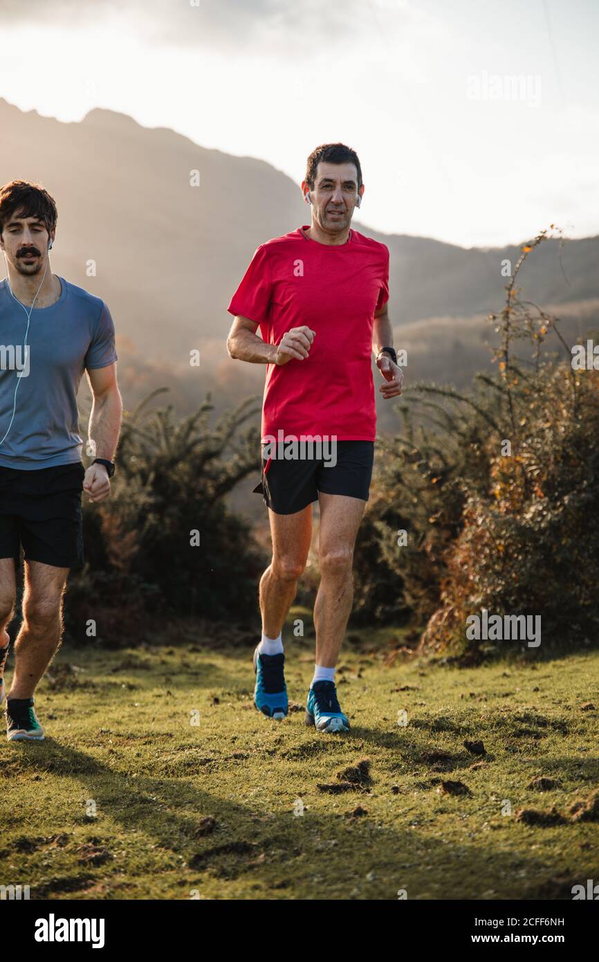 Starke aktive Männer in Sportbekleidung laufen zusammen auf grünem Gras In den Bergen im sonnigen Herbsttag Stockfoto