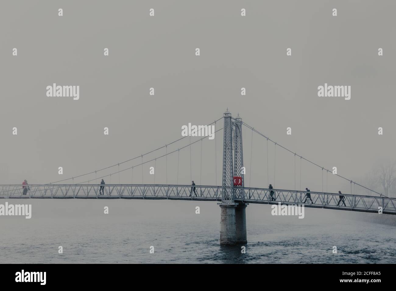 Menschen, die durch den Fluss auf einer modernen Brücke mit Nebel auf wolkiger Tag Stockfoto