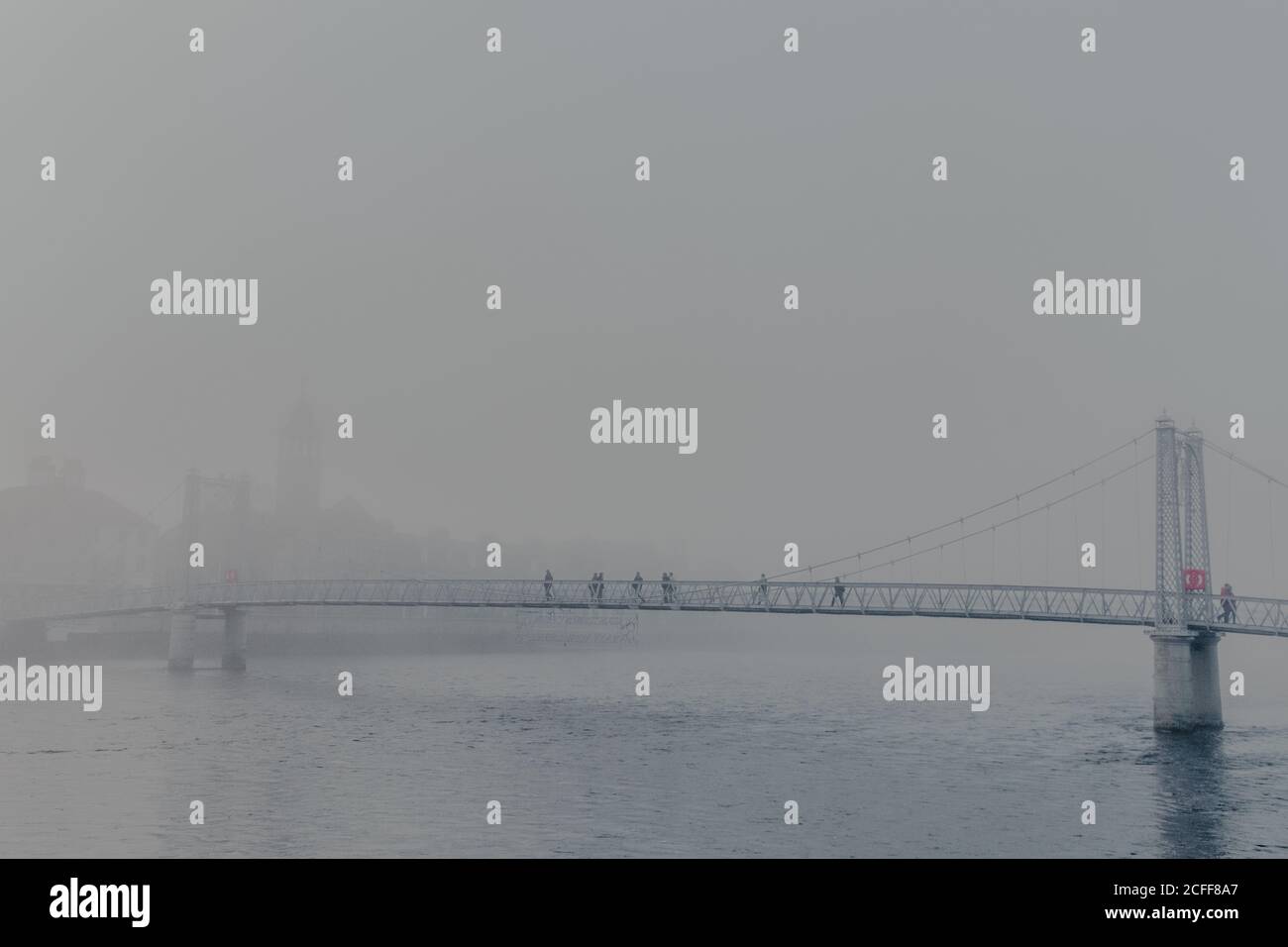 Menschen, die durch den Fluss auf einer modernen Brücke mit Nebel auf wolkiger Tag Stockfoto