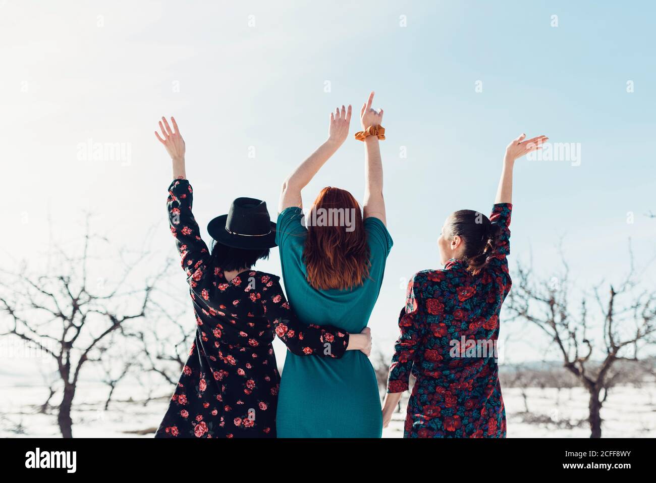 Fröhliche junge Freundinnen in bunten Kleidern mit Spaß und stehend Auf Schnee im Winterfeld mit Baumbepflanzung Stockfoto