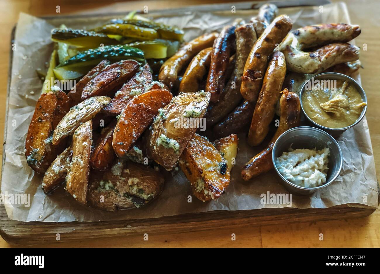 Wiener Würstchen mit Bratkartoffeln und Knoblauch auf einem Holzteller um Holzhintergrund. Kreative Komposition. Gesundes Lifestyle-Konzept. Stockfoto