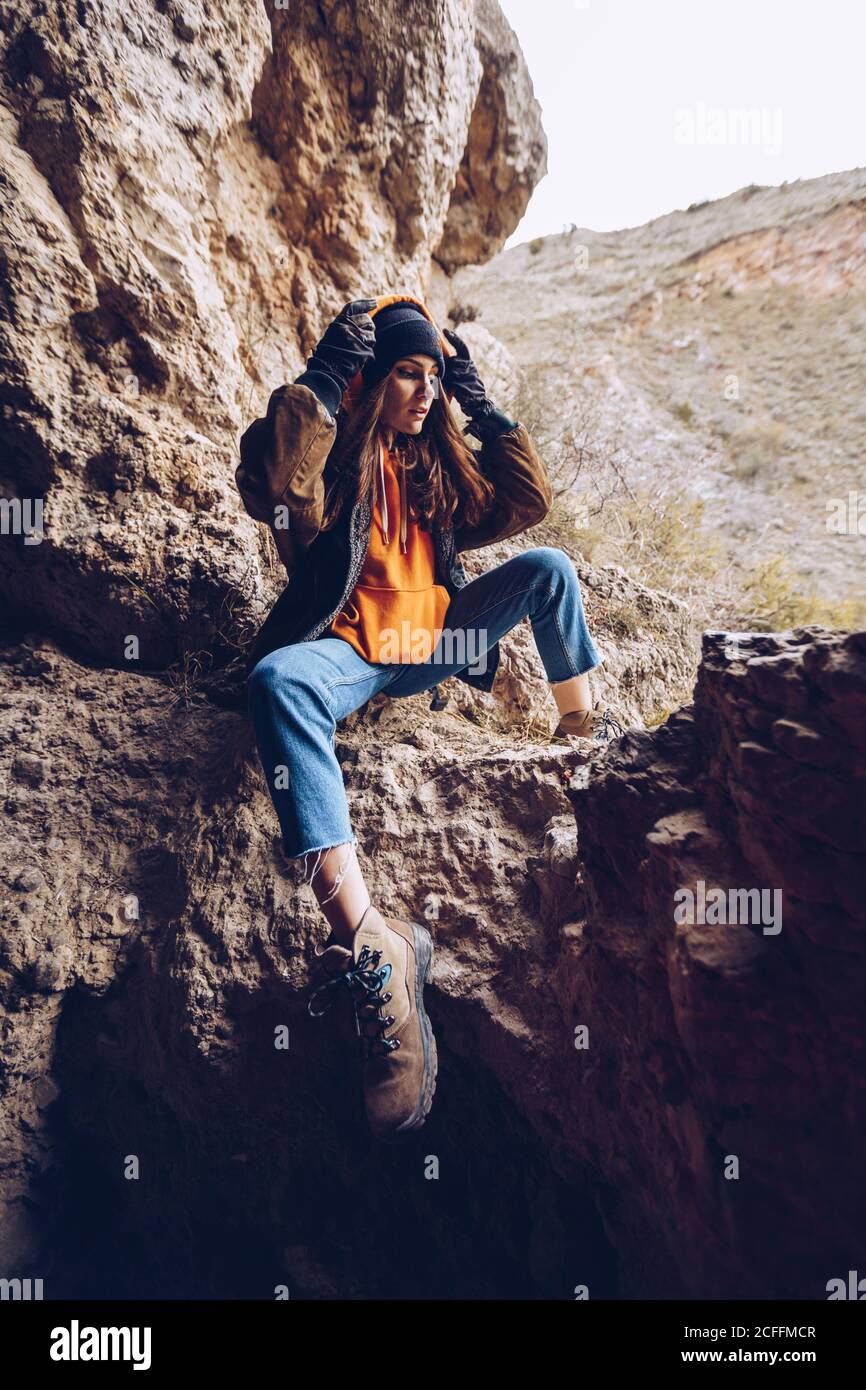 Ruhige Frau in warmer Kleidung, die sich an der Hand lehnt und auf einer Bergklippe sitzt Stockfoto