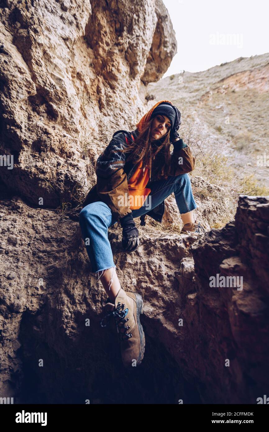 Ruhige Frau in warmer Kleidung, die sich an der Hand lehnt und auf einer Bergklippe sitzt Stockfoto