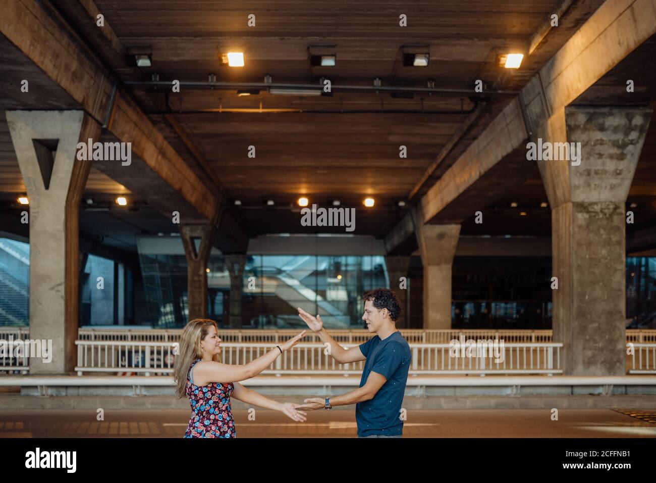 Seitenansicht eines schönen Paares, das Zeit zusammen verbringt und spielt Clapping Hände Spiel unter großer Brücke in Abendlicht auf Stadtstraße Stockfoto