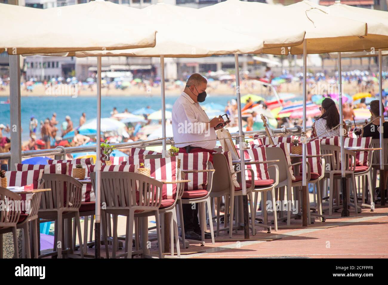 Las Palmas, Gran Canaria, Kanarische Inseln, Spanien. September 2020. Ein Kellner überprüft sein Telefon, während er an einem heißen Tag am Stadtstrand in Las Palmas auf Kunden wartet. Da britische und deutsche Staatsangehörige bei ihrer Rückkehr aus Spanien in Quarantäne gehen müssen, ist die Zahl der Touristen gesunken. Auf den Kanarischen Inseln ist ein Anstieg der Covid-Fälle zu verzeichnen, und auf den Kanarischen Inseln wurde gestern, 381, eine Rekordzahl von täglichen Fällen verzeichnet. Die August-Statistik für die Kanarischen Inseln betrug 4,469 neue Fälle (durchschnittlich 144 Fälle pro Tag), davon 70% auf Gran Canaria, wobei Las Palmas der Hotspot war. Kredit: Alan Dawson/A. Stockfoto