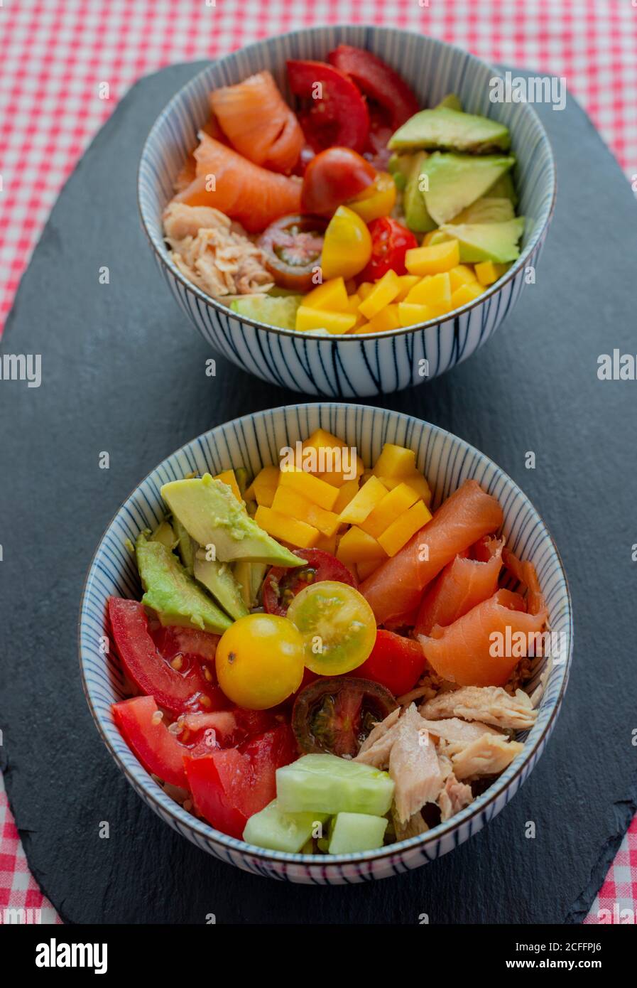 Schüsseln mit gehacktem frischem Gemüse und Fleisch von Lachs und Huhn auf dem Tisch in der Küche zum Mittagessen Stockfoto