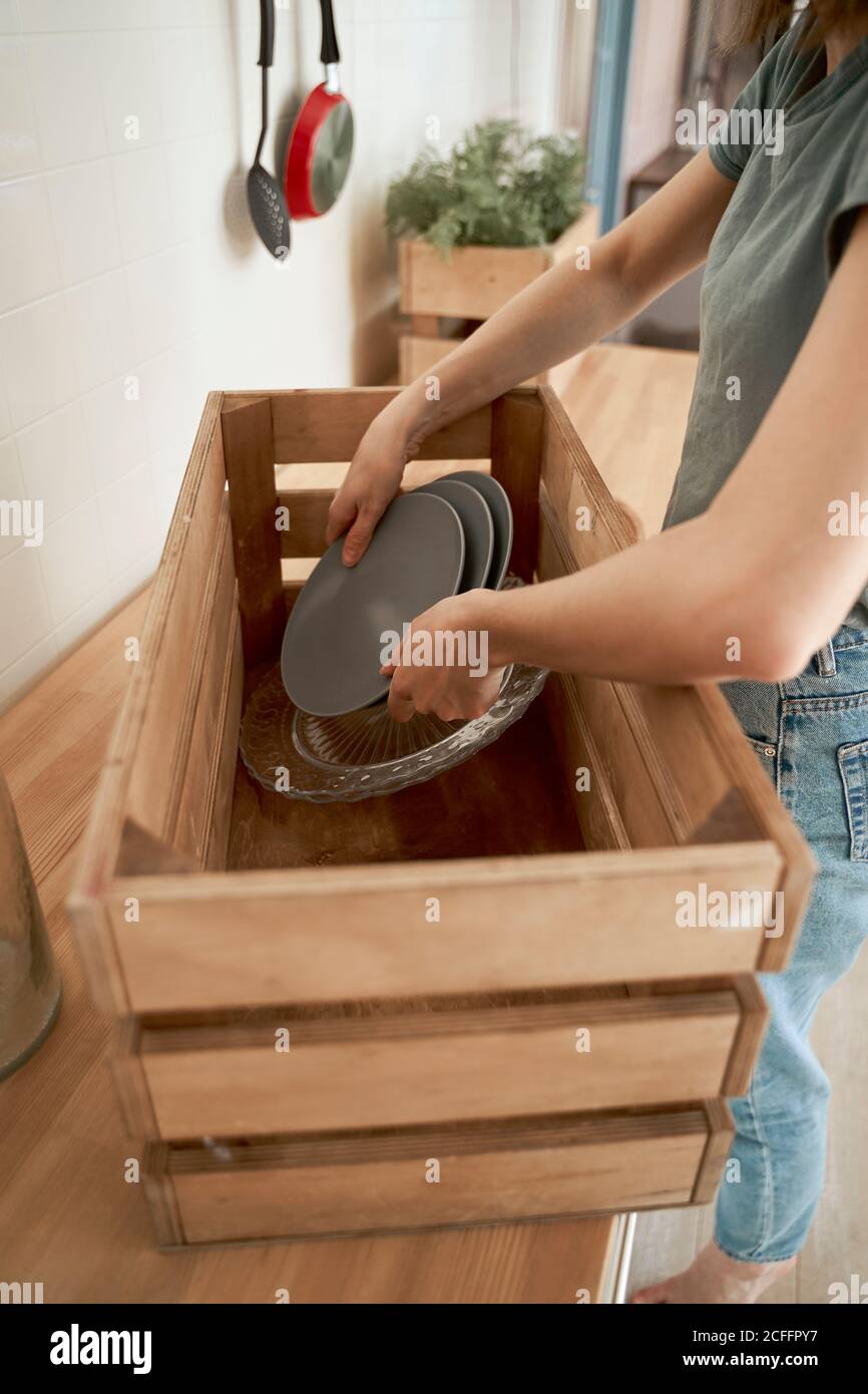 Crop Frau in legerer Kleidung Verpackung Hause Geschirr in Holzkiste an der Theke in der Küche Stockfoto