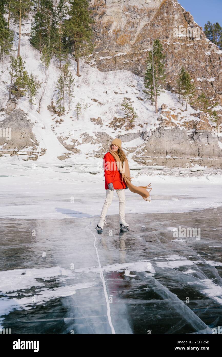 Glücklich aktive Frau in warmen Sportbekleidung Skating auf Eis Sibirischer Fluss neben Felsen mit Schnee und Kiefern bedeckt Bäume Stockfoto
