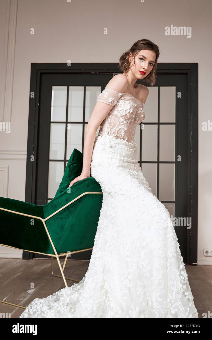 Chic ruhige Frau in weißem Hochzeitskleid auf Sessel lehnt Stockfoto
