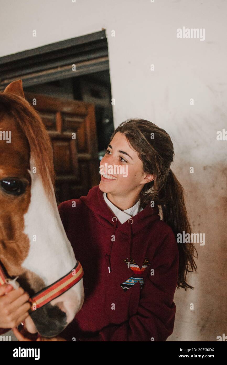 Teenager-Mädchen umarmen mit kleinen Pony in niedlichen Hut auf Ohren stehen im Stall Stockfoto