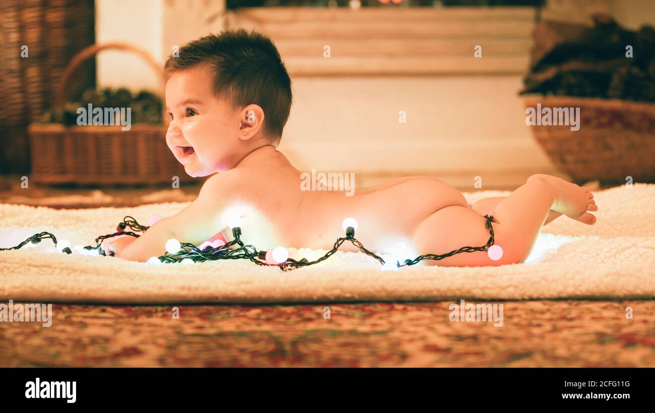 Baby spielt mit leichter Girlande am Weihnachtstag Stockfoto