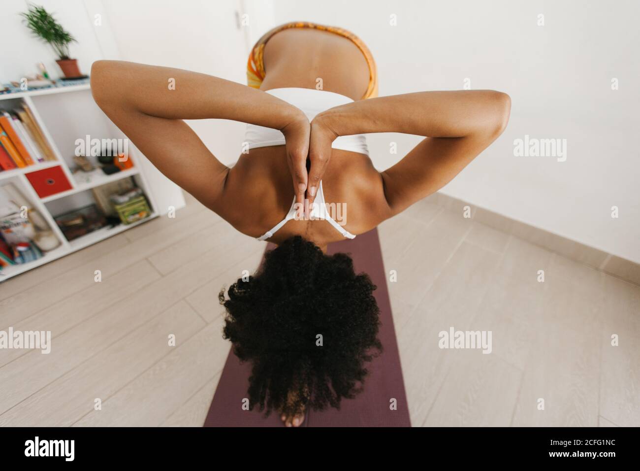Rückansicht einer anonymen afroamerikanischen attraktiven jungen Frau, die im hellen Raum mit gefalteten Händen hinter dem Rücken eine Yogaposition durchführte Stockfoto