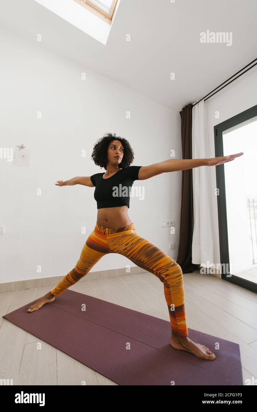 Afroamerikanische attraktive junge Frau, die im hellen Raum Yoga-Haltung mit gestreckten Armen auf Matte durchführt Stockfoto