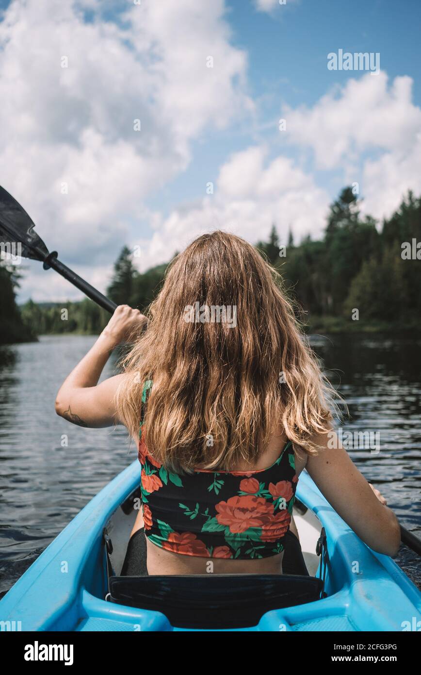 Rückansicht der anonymen weiblichen Reisenden in Lebensweste sitzen im Boot während der Flusserkundung gegen bewölkten Himmel im La Mauricie Nationalpark in Quebec, Kanada Stockfoto