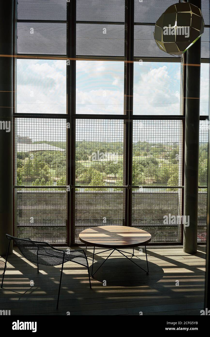 Loungebereich mit rundem Holztisch und Metallstuhl Hohe Fenster mit Gitter in kontrastreicher Beleuchtung in Library Texas Stockfoto