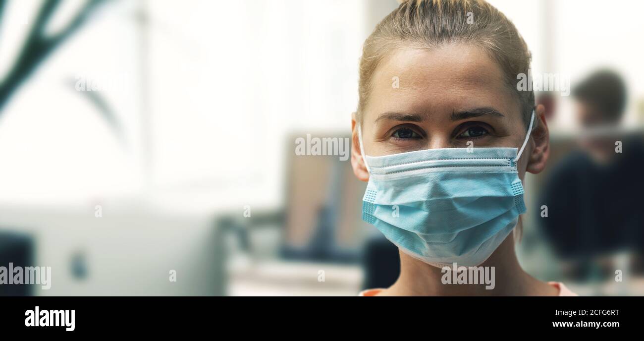 Junge Frau im Büro trägt Gesichtsmaske Nahaufnahme. Soziale Distanzierung und Sicherheit bei der Arbeit während Virus-Pandemie. Copy space Stockfoto