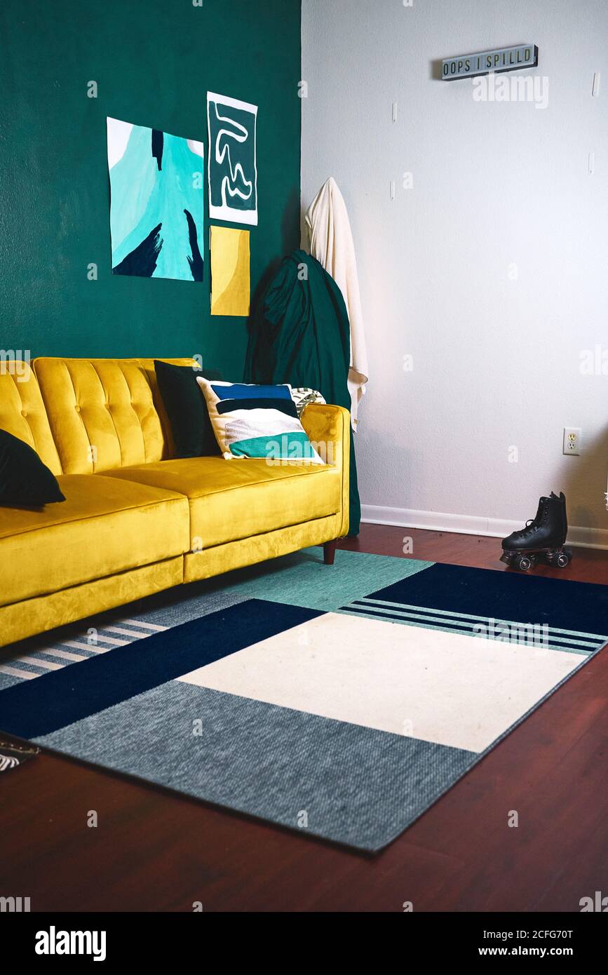 Interieur des stilvollen Wohnzimmer mit kreativer Innenausstattung einschließlich hell Gelbes Sofa und Teppich auf Holzboden mit Einzelrolle Stiefel in der Nähe der Wand platziert Stockfoto