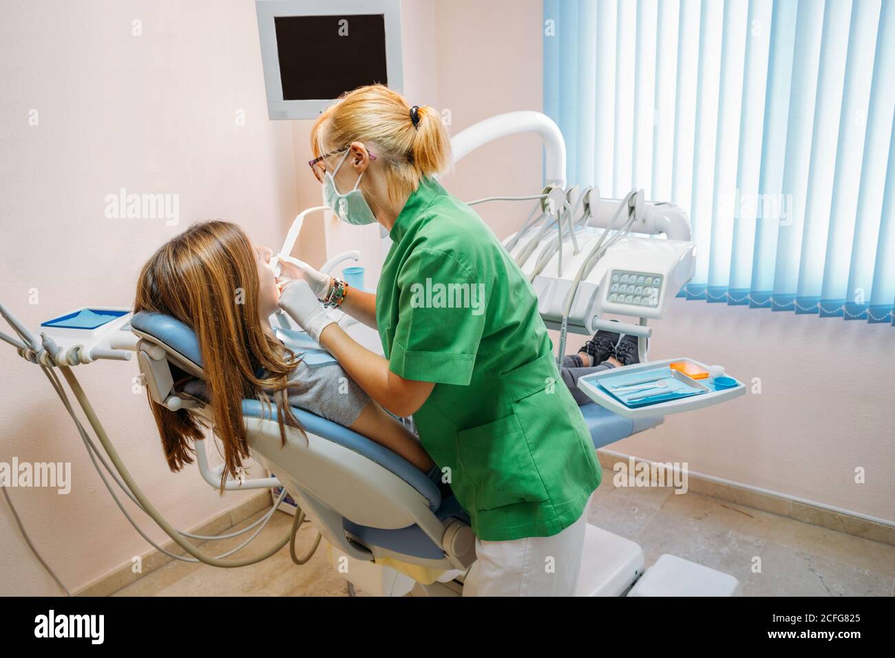 Fokussierter Arzt mittleren Alters in grüner Uniform, der die Mundhöhle der Frau im Zahnarztstuhl untersucht Stockfoto