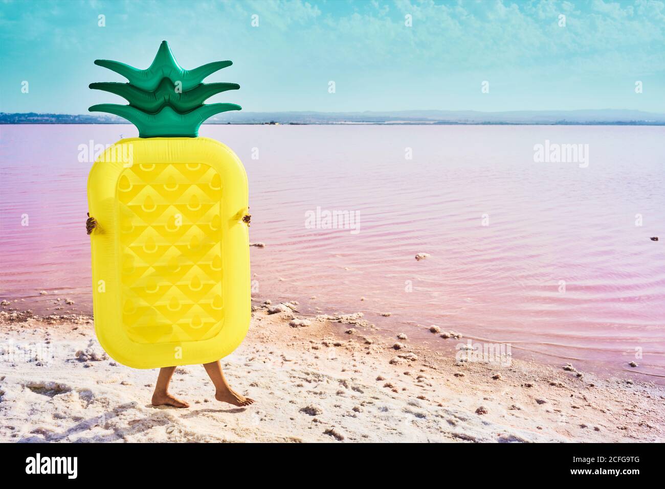 Gebräunte Frau, die an der Küste mit Luftmatratze in Form von Ananas in der roten Lagune läuft Stockfoto