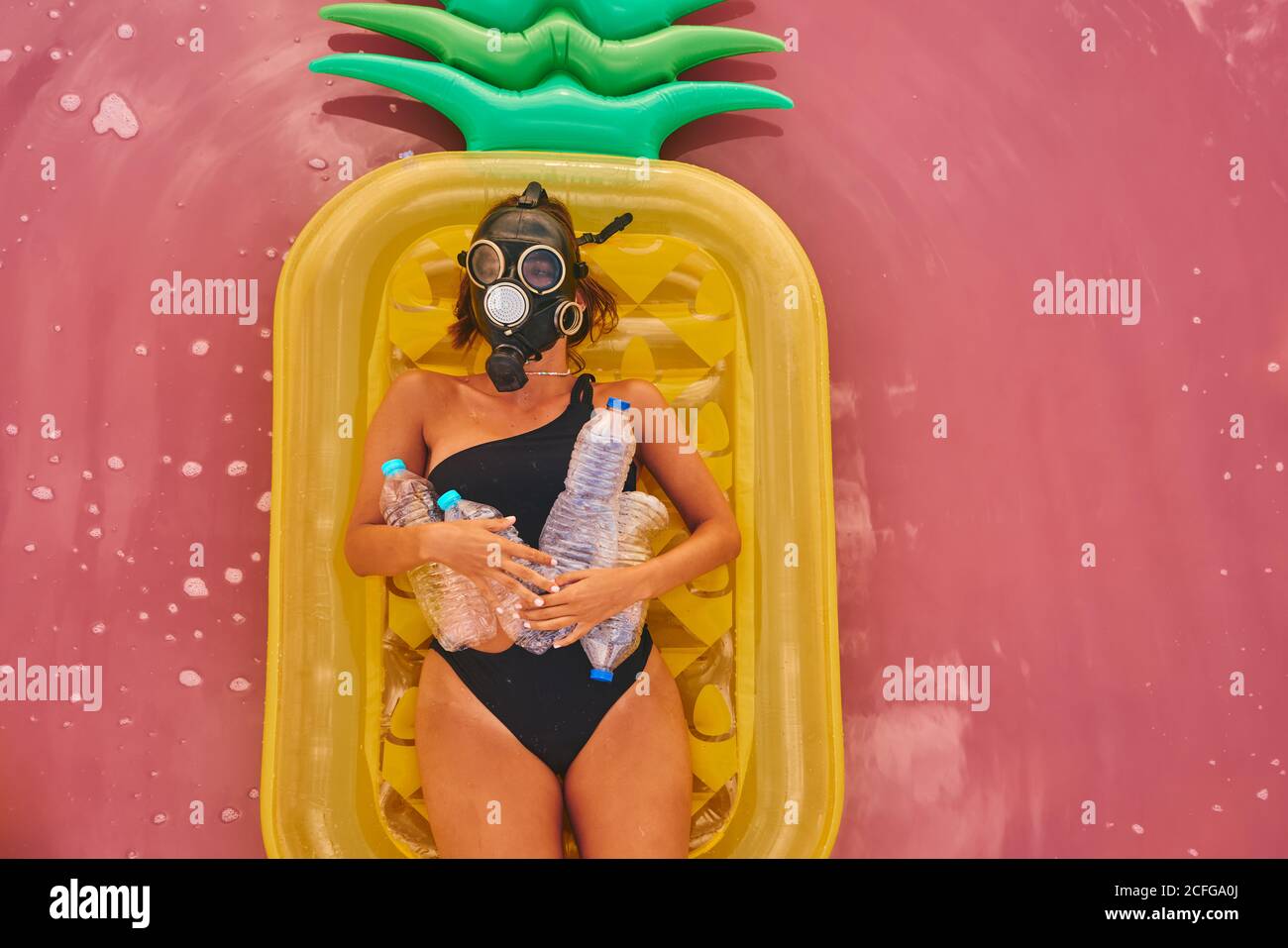 Ansicht von oben auf einer Frau in einem Atemschutzgerät mit Plastikflaschen, die auf einer aufblasbaren Ananas-Matratze im roten Wasser der tropischen Lagune liegen Stockfoto