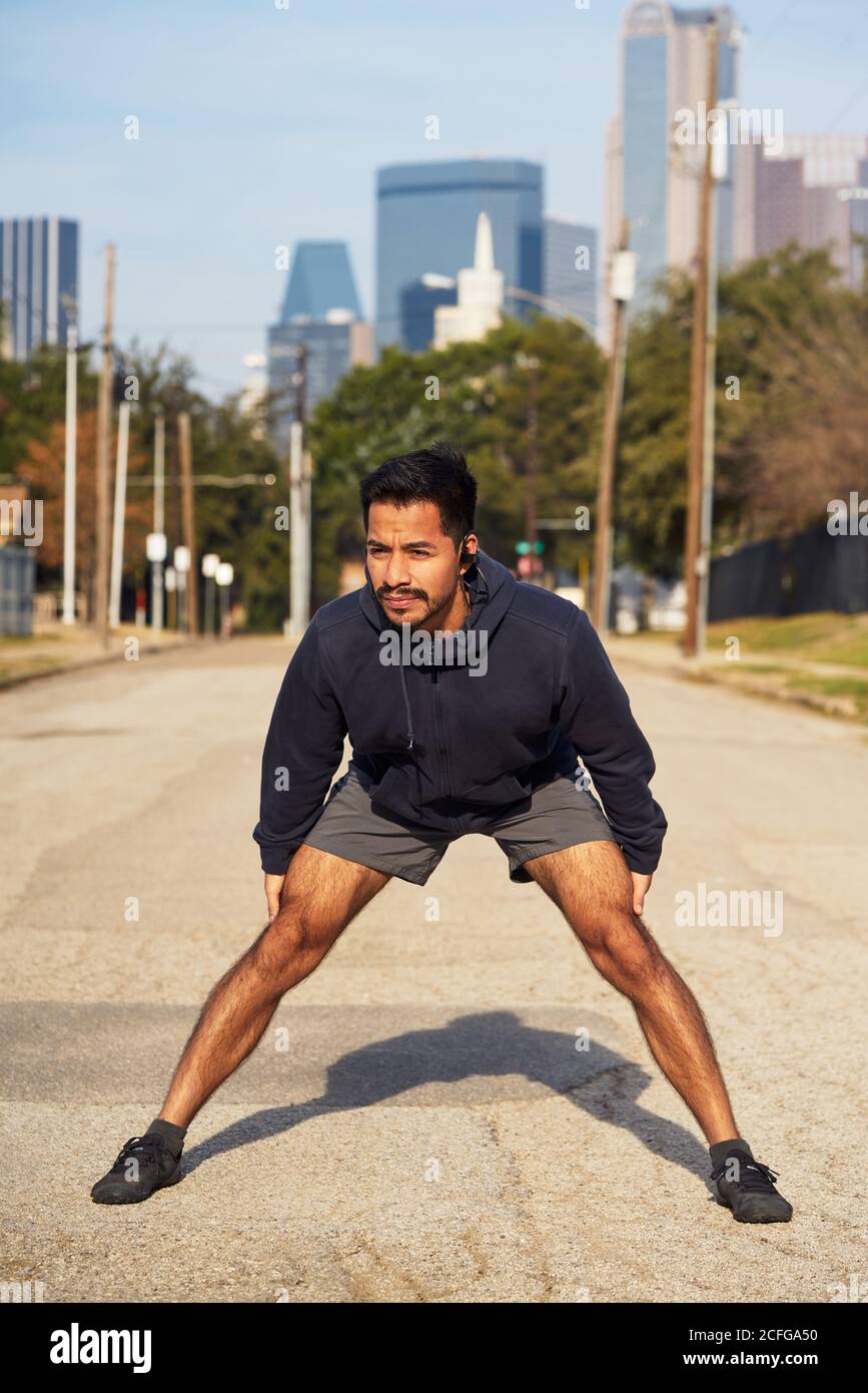 Hispanische männliche Turnerin in aktiver Kleidung stehend und streckend Arm zu gegenüberliegenden Fuß in der Innenstadt von Dallas, USA Stockfoto