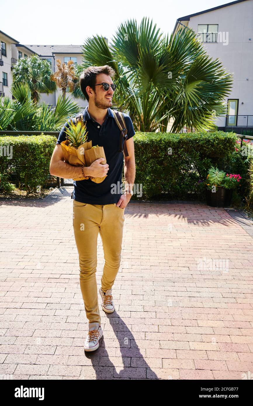 Fröhlicher Mann in Sonnenbrille im trendigen Outfit auf der Straße stehend Mit Einkaufstaschen Stockfoto
