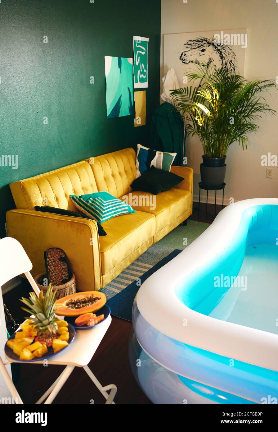 Hoher Winkel der kreativen Wohnung mit aufblasbarem Pool für zu Hause Party und frische tropische Früchte auf Stuhl gelegt Stockfoto