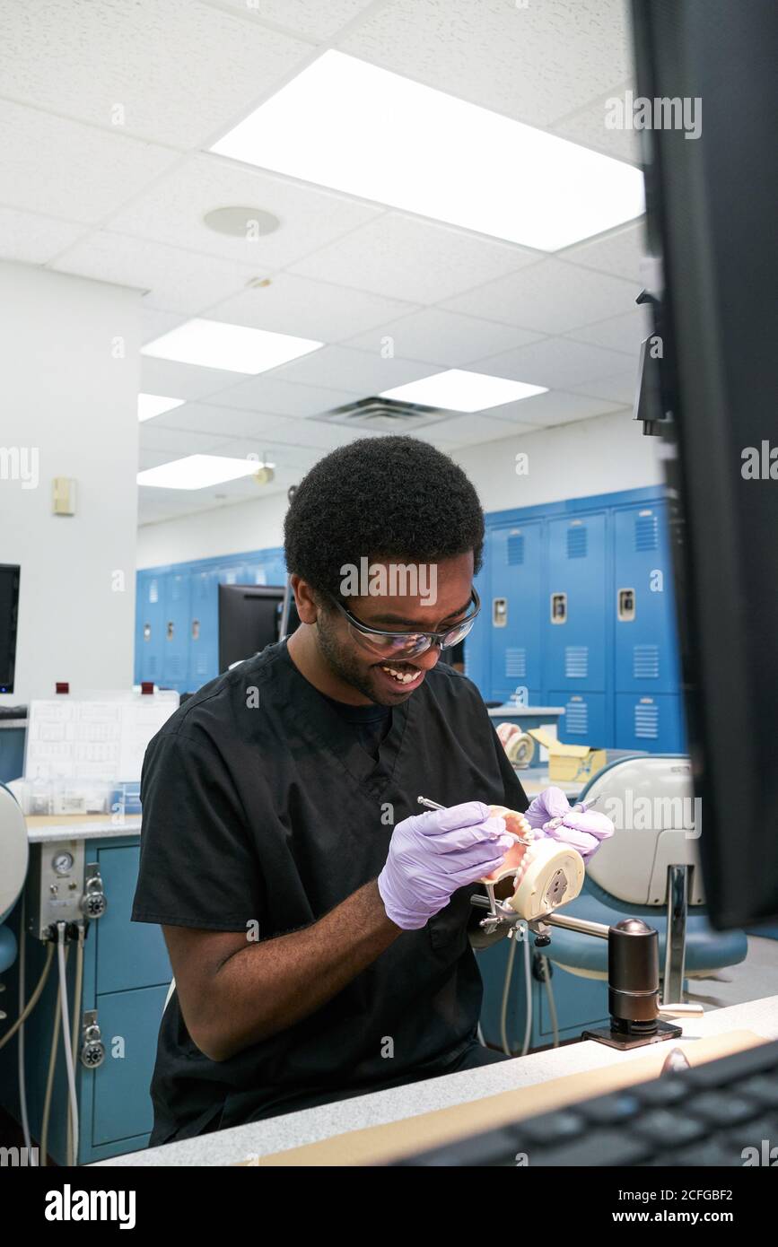 African American Kerl in Latexhandschuhe mit Mund Spiegel und Sonde zur Überprüfung falscher Zähne bei der Arbeit im modernen Labor Stockfoto