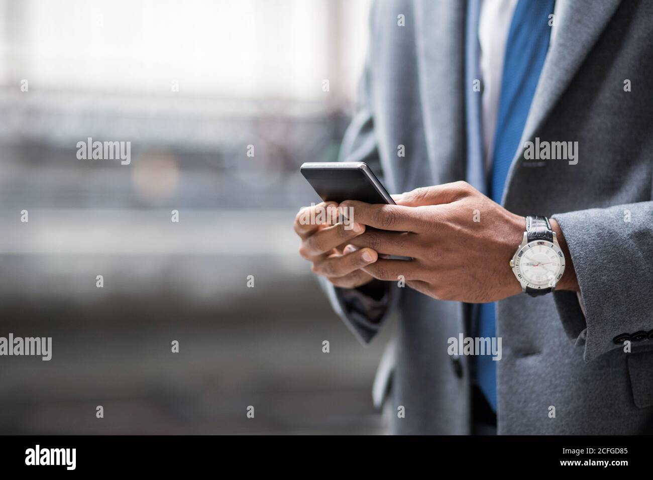 Gesichtslose Aufnahme von schwarzen Geschäftsmann in Anzug und Uhr mit Smartphone draußen. Stockfoto