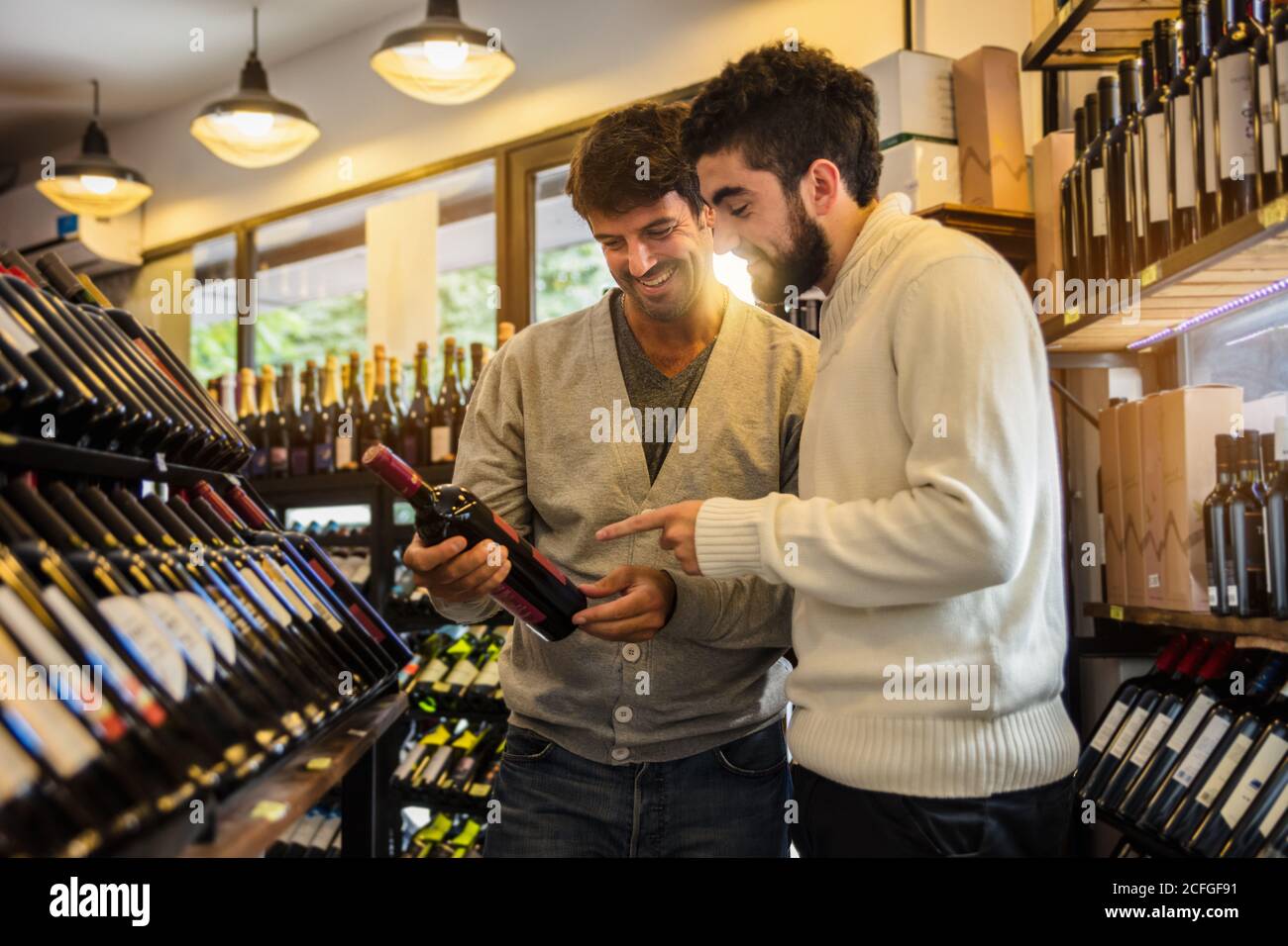 Seitenansicht von eleganten lachenden Männern, die das Sortiment in Regalen des Weinkellers erkunden und die Wahl treffen. Stockfoto