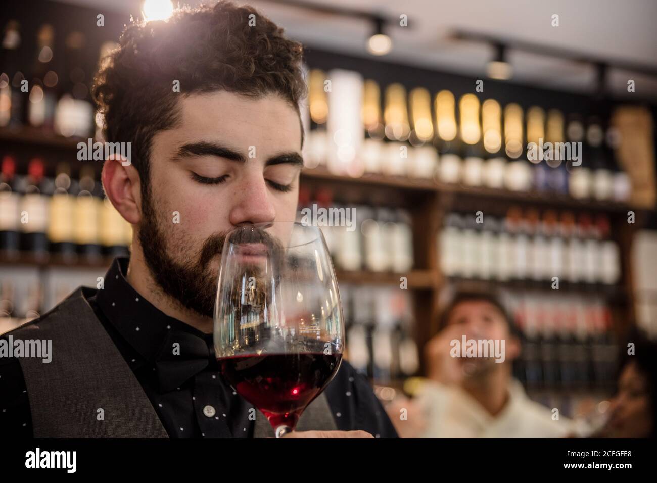 Bärtiger Sommelier in elegantem Outfit mit geschlossenen Augen und duftenden Rotwein im Glas. Stockfoto