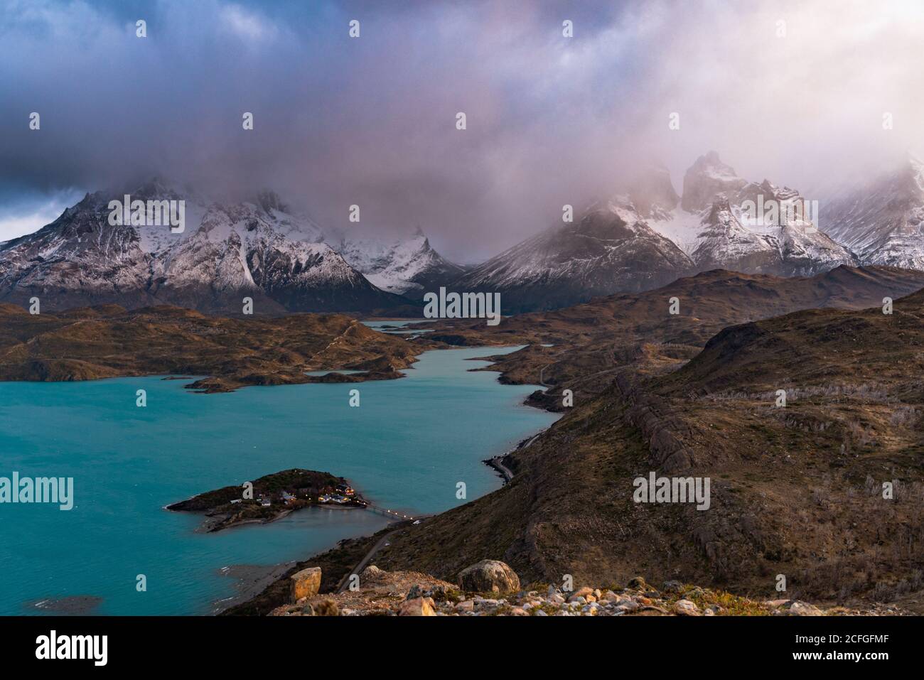 Von oben atemberaubende Landschaft von ruhigen Fluss mit türkisfarbenem Wasser Im Hochland gegen verschneite Berge Gipfeln inmitten dramatischer Wolken Stockfoto