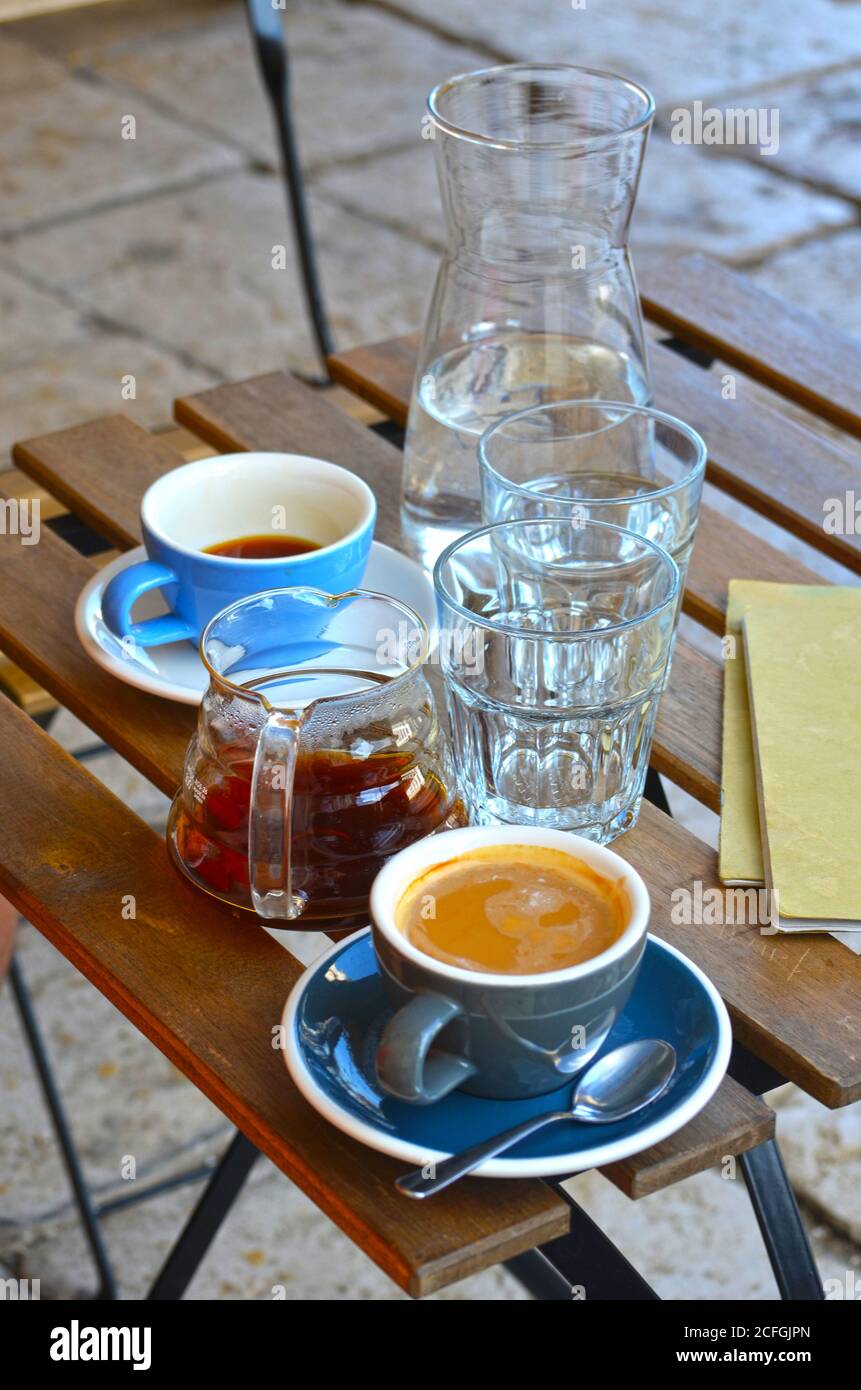 Filterkaffee und Espresso Lungo in blauen Tassen mit Krug Von Wasser auf einem Holztisch im Freien Stockfoto