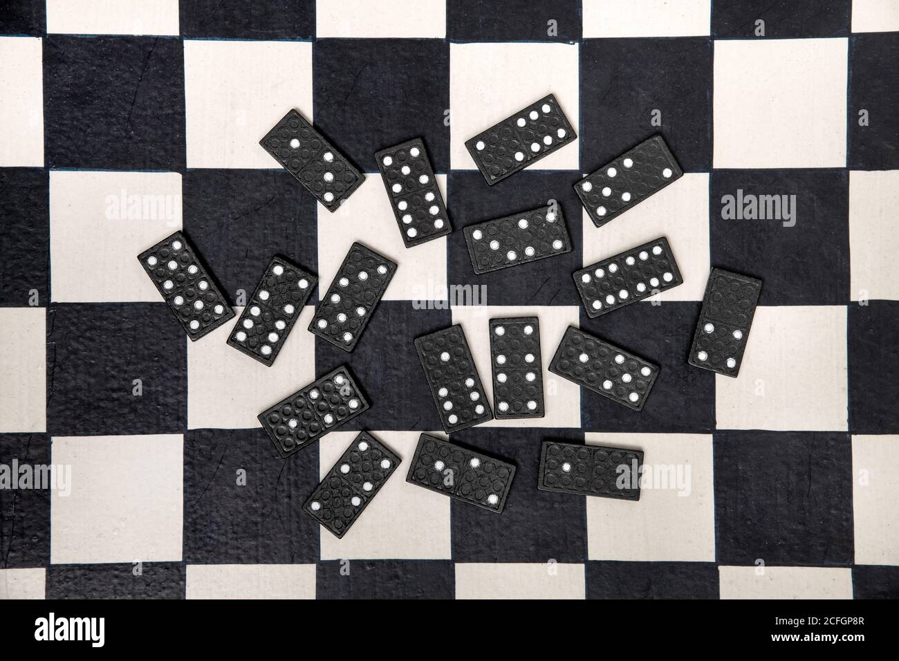 Zufällig verstreute schwarze Domino-Fliesen auf einem schwarz-weiß Schachbrett von oben betrachtet in einem Konzept der persönlichen Unterhaltung Stockfoto