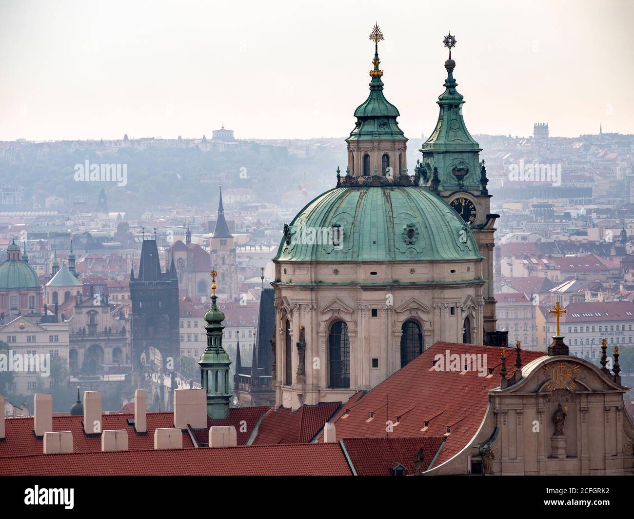 Prag von der Burg: Ein frühmorgens nebliger Überblick über die Stadt und ihre Türme vom Schlossgelände. Die Kuppel des St. Nikolaus dominiert das Vorland mit der Karlsbrücke in der Mitte. Stockfoto